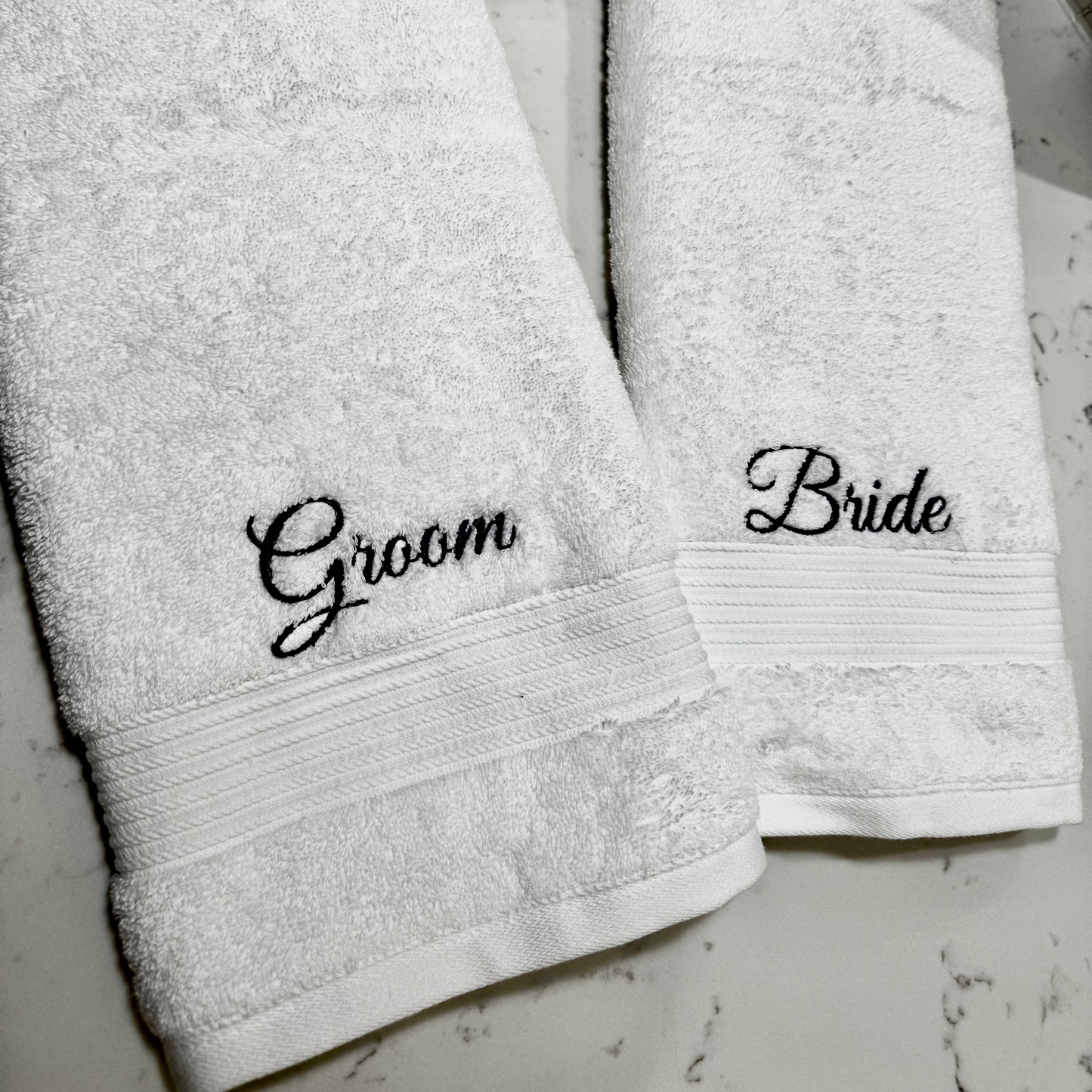 Two white towels with 'Groom' and 'Bride' embroidery on a light gray background.