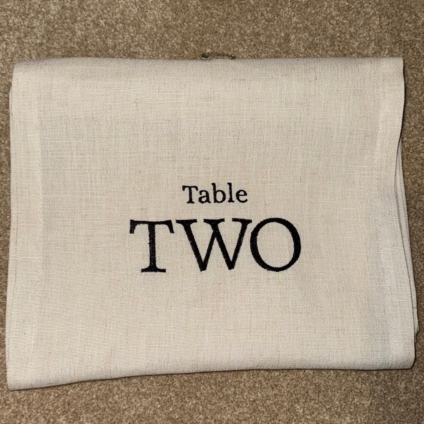 Folded beige table runner with 'Table TWO' text on a brown surface