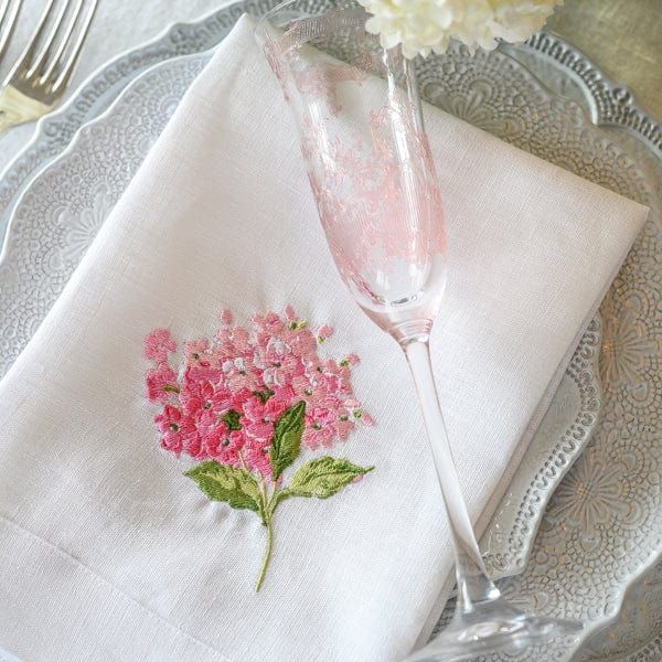 Napkin with floral embroidery holding a glass on a decorative plate.