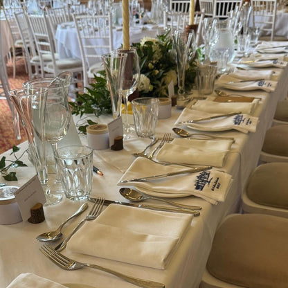 Dining table set for a formal event with white tablecloths, silverware, and floral centerpieces.