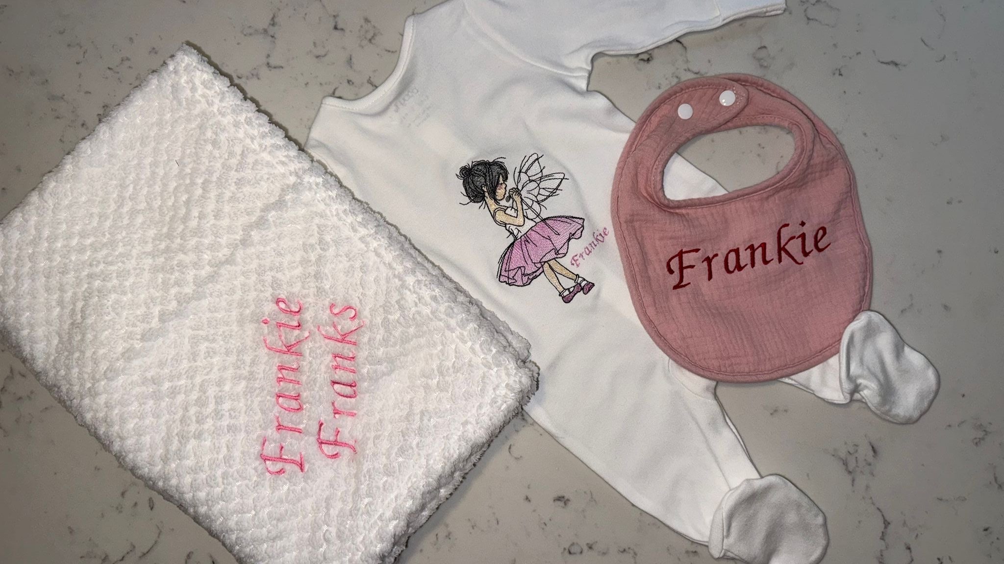 Baby clothing set with bib, onesie, and blanket featuring 'Frankie Franks' branding on a textured surface.