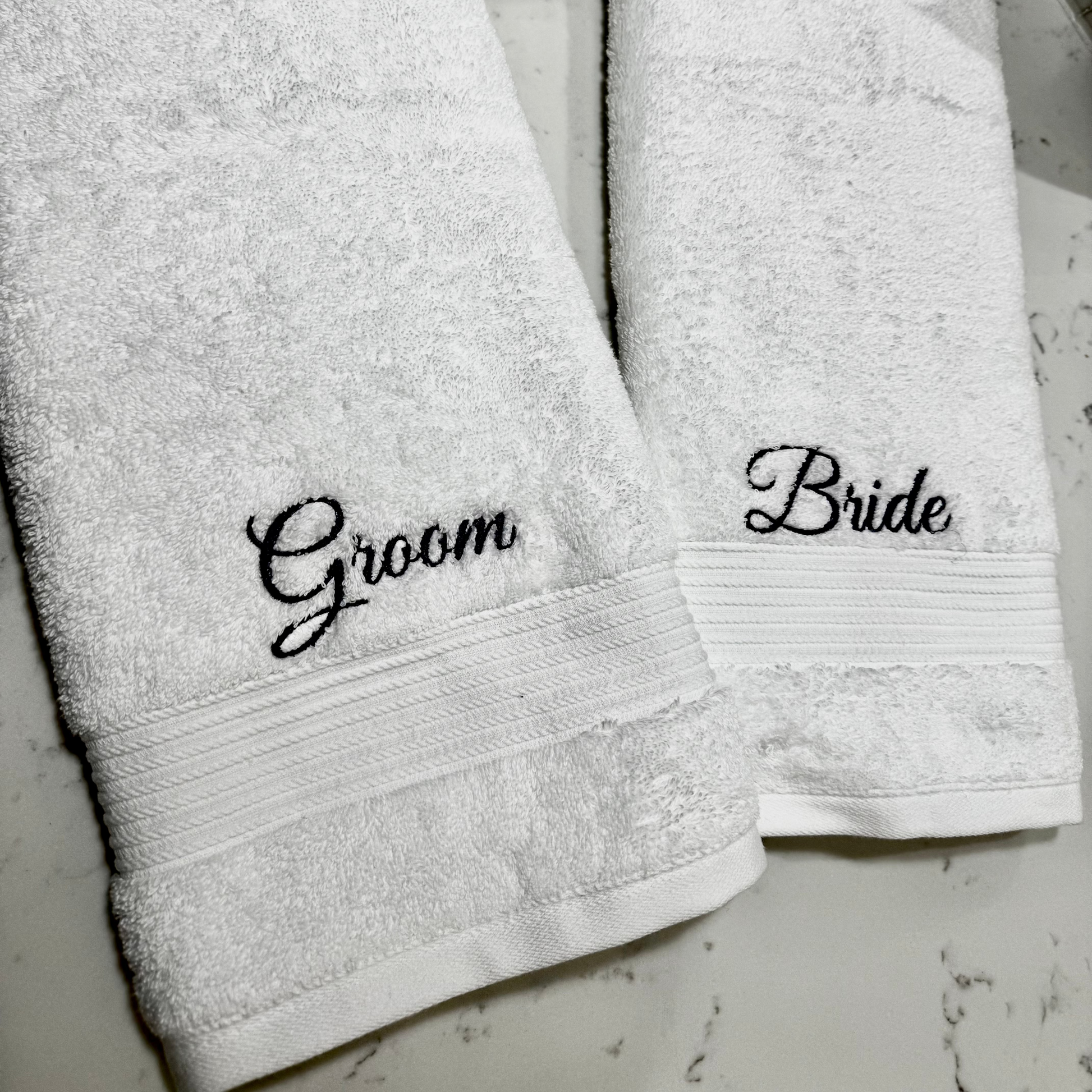 Two white towels with 'Groom' and 'Bride' embroidery on a light gray background.