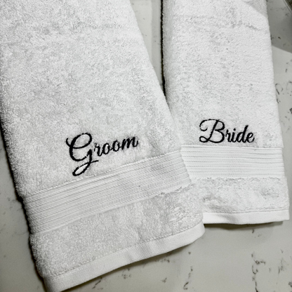 Two white towels with 'Groom' and 'Bride' embroidery on a light gray background.