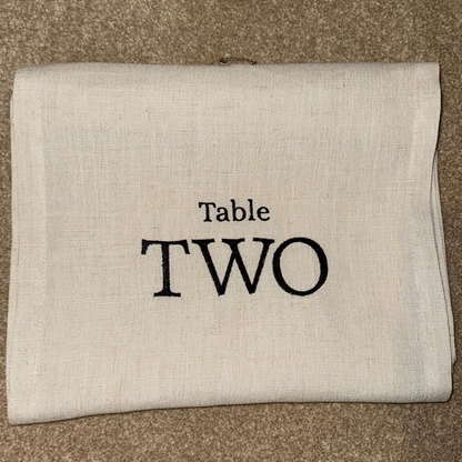 Folded beige table runner with 'Table TWO' text on a brown surface