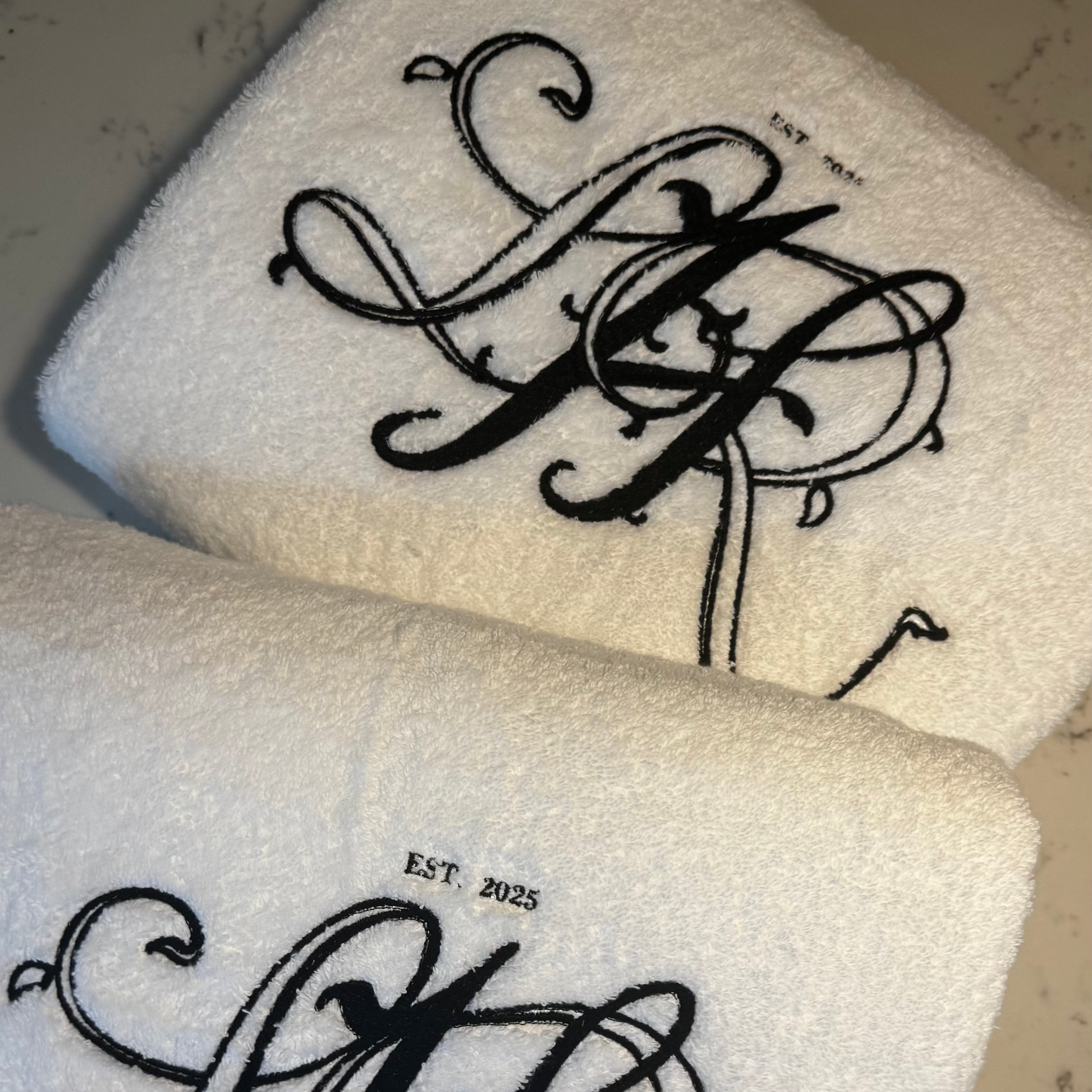 Two white towels with black monogram designs on a marble surface