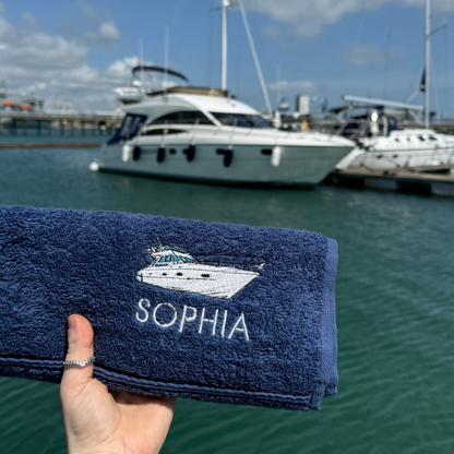Navy blue towel with 'SOPHIA' and a logo held in front of a marina with boats.