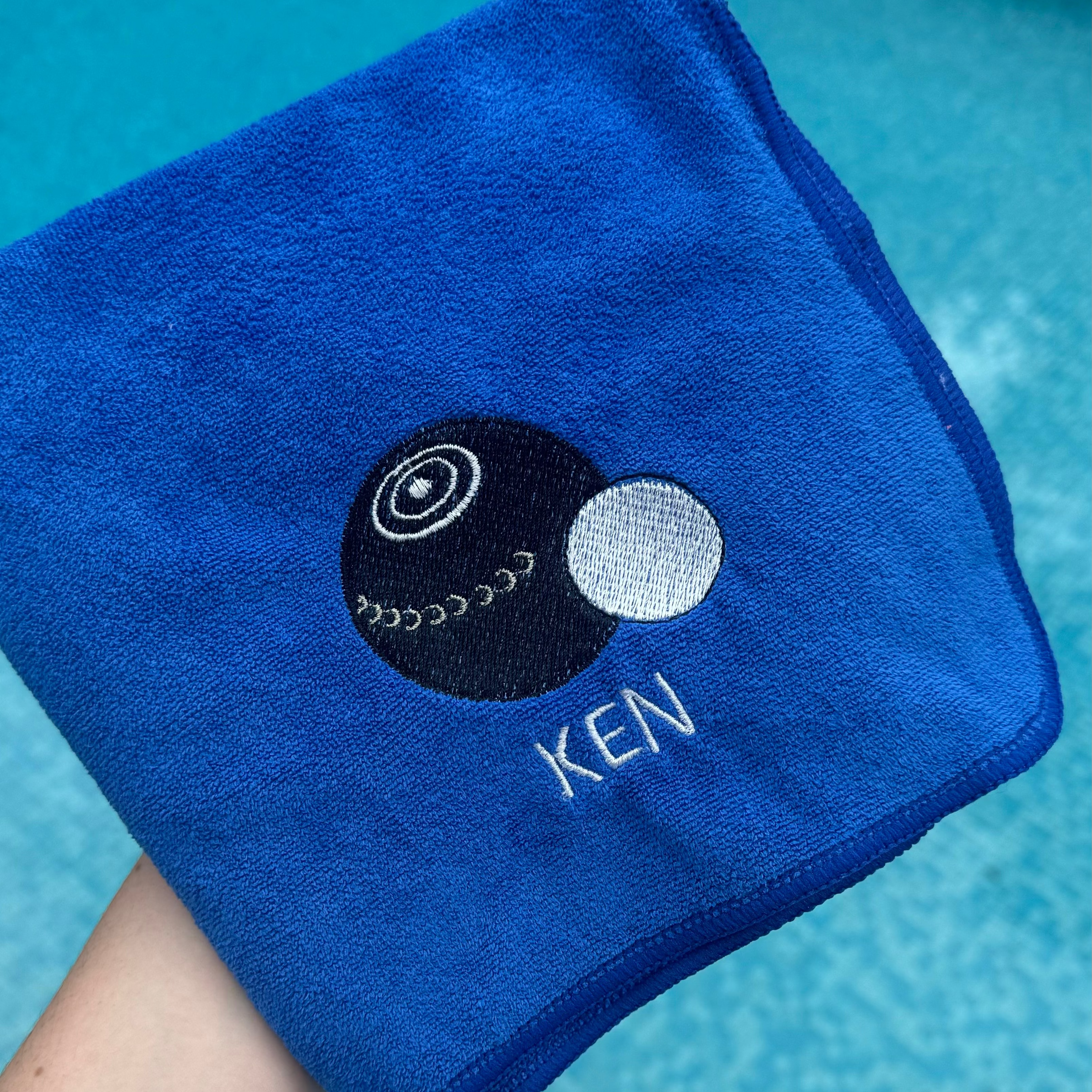 Blue towel with a logo and 'KEN' text held by a person against a pool background